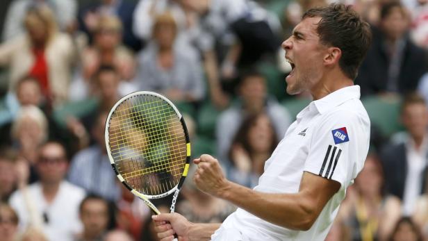 Ein Tennisspieler jubelt mit erhobener Faust und Tennisschläger vor einer Zuschauermenge.