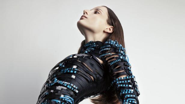 Eine Frau präsentiert ein futuristisches, schwarzes Kleid mit blauen Akzenten.