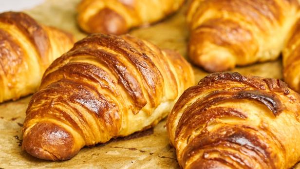 Mehrere goldbraune Croissants liegen auf Backpapier.
