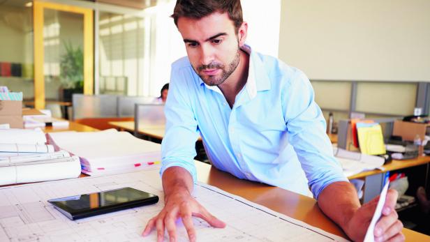 Male Architect With Digital Tablet Studying Plans In Office