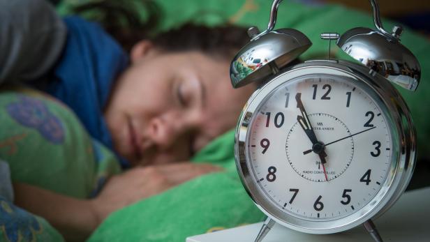 Eine Frau schläft, während ein Wecker auf dem Nachttisch steht.