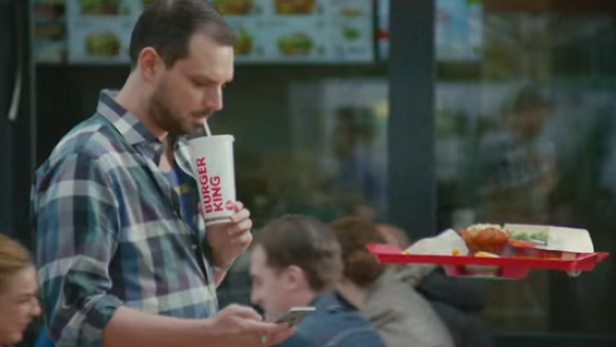 Ein Mann trinkt aus einem Burger King Becher und schaut auf sein Handy.