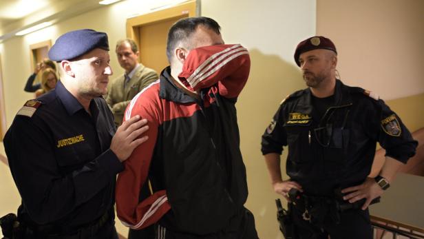 Ein Mann wird von zwei Justizbeamten abgeführt, sein Gesicht ist verdeckt.