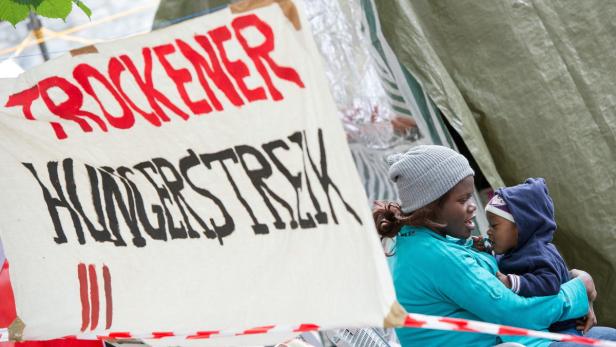 epa03762389 A mother and child sit next to a banner reading &#039;Dry Hunger Strike&#039; as asylum seekers refuse to drink water as part of a hunger strike at an outdoor protest camp in Munich, Germany, 27 June 2013. According to media reports, for five days about 100 asylum seekers have been on hunger strike in protest for better rights for refugees. Some of them have been taken to hospital. EPA/MARC MUELLER