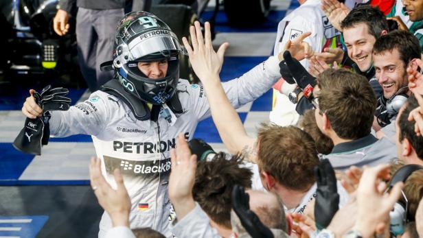 Ein Formel-1-Fahrer in Rennkleidung feiert mit seinem Team.