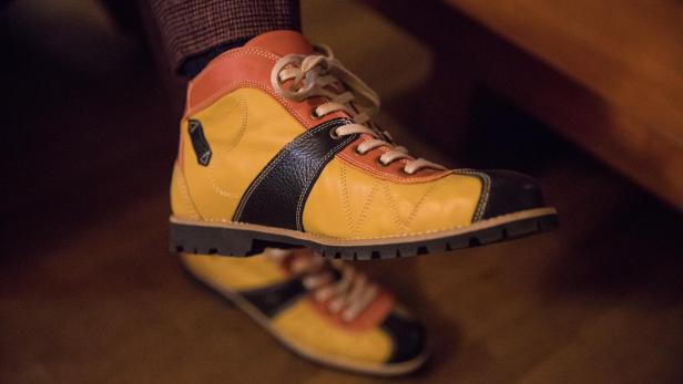 Ein gelb-orangefarbener Lederschuh mit schwarzen Akzenten wird präsentiert.