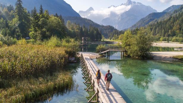 Zwei Wanderer überqueren eine Holzbrücke in einer malerischen Berglandschaft.