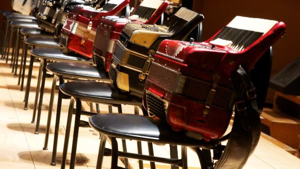 Mehrere Akkordeons stehen auf Stühlen auf einer Bühne bereit.