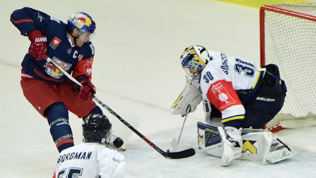 Ein Eishockeyspieler in roter und blauer Uniform schießt auf das Tor, das von einem Torwart verteidigt wird.