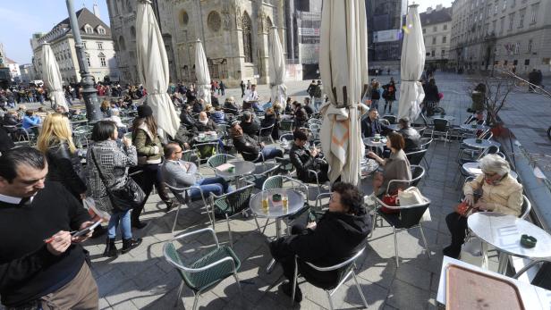 Viele Menschen sitzen an Tischen in einem Straßencafé vor dem Stephansdom in Wien.
