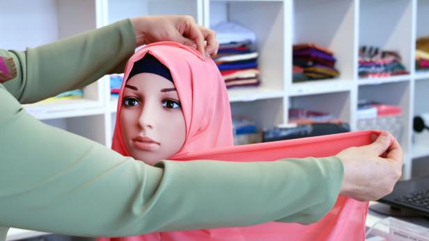 Ein Schaufensterpuppenkopf bekommt ein rosa Kopftuch angelegt.