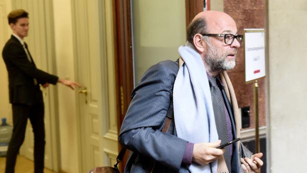 Ein Mann mit Brille und Schal verlässt ein Gebäude, während ein anderer eine Tür öffnet.