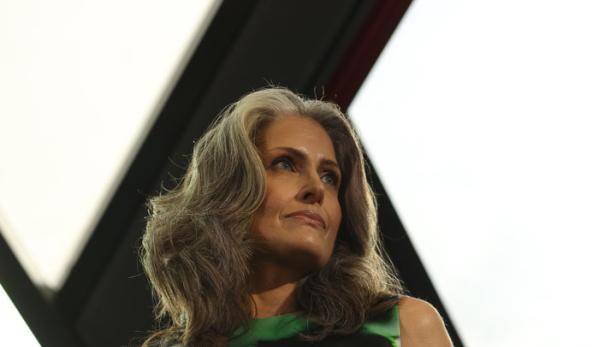 Eine Frau mit grauem Haar trägt ein grünes Kleid mit einem weißen Gürtel.