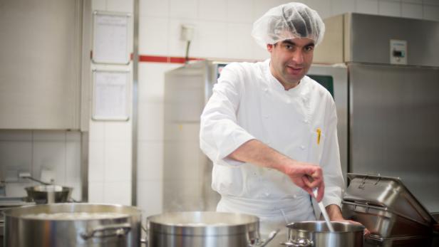 Ein Koch rührt in einer professionellen Küche in einem Topf.