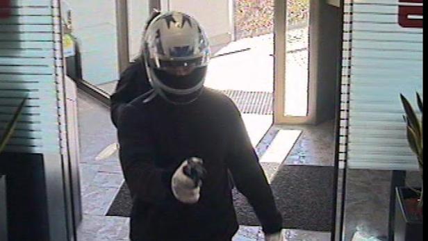 Eine Person mit Motorradhelm und Waffe betritt ein Gebäude.