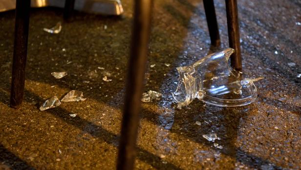 Ein zerbrochenes Glas liegt auf dem Boden unter einem Tisch.