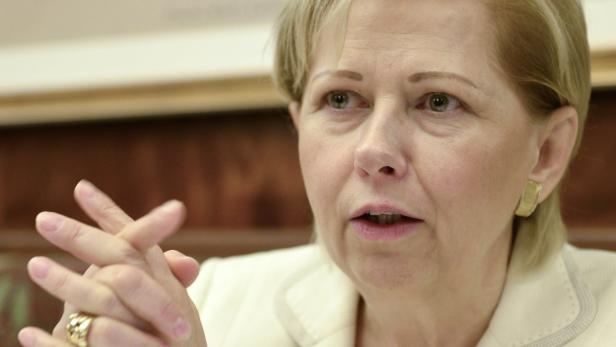 Eine Frau mit blonden Haaren spricht mit verschränkten Händen.