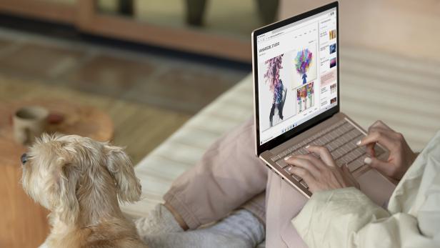 Eine Frau arbeitet an einem Laptop, während ein Hund daneben sitzt.