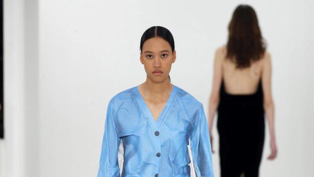 Ein Model präsentiert eine blaue Weste und eine große braune Ledertasche von Loewe.