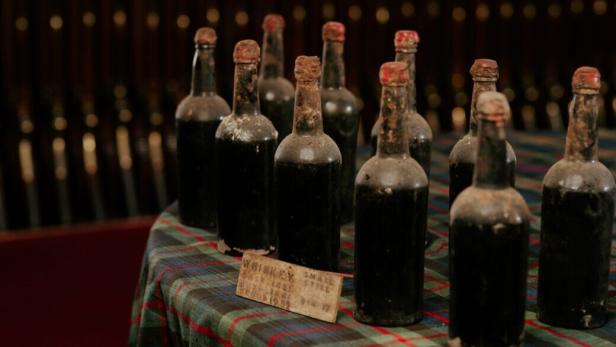 Alte Whiskeyflaschen stehen auf einem karierten Tuch.