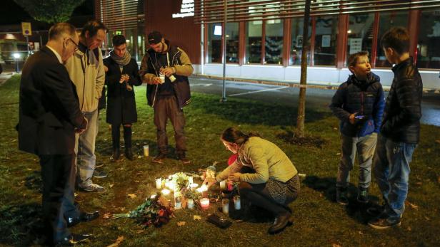 Menschen zünden Kerzen an einem improvisierten Denkmal im Freien an.