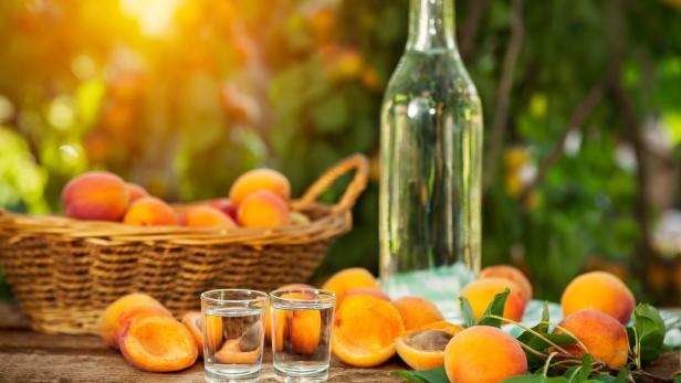 Aprikosen, Schnapsgläser und eine Flasche auf einem Holztisch.