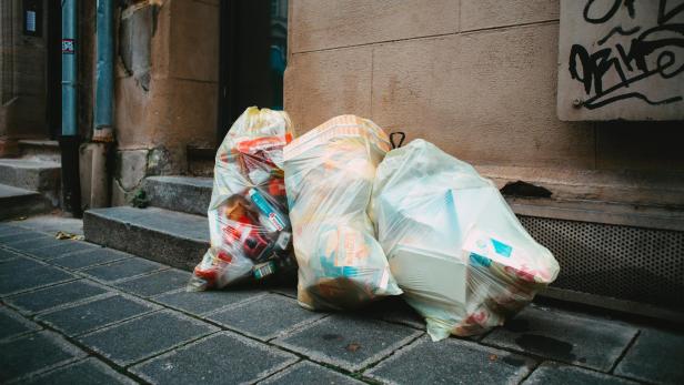Müllsäcke stehen auf einem Bürgersteig vor einer Hauswand.
