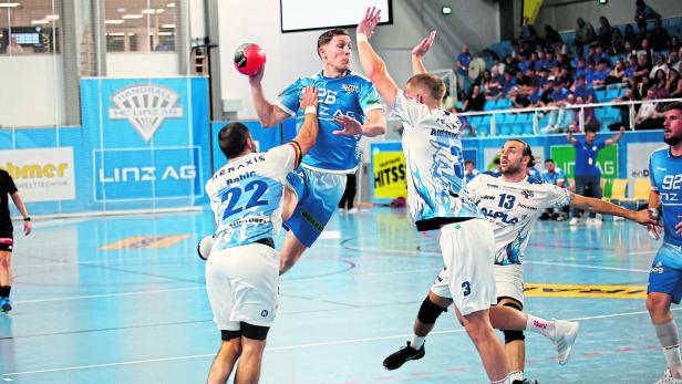 Ein Handballspieler springt hoch, um den Ball zu werfen, während andere Spieler zusehen.