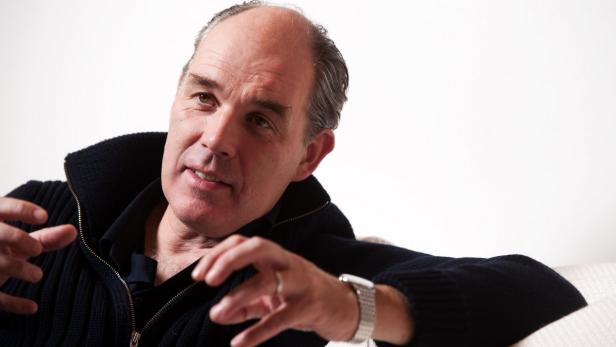 Ein Mann mit einer dunklen Strickjacke gestikuliert mit seinen Händen.