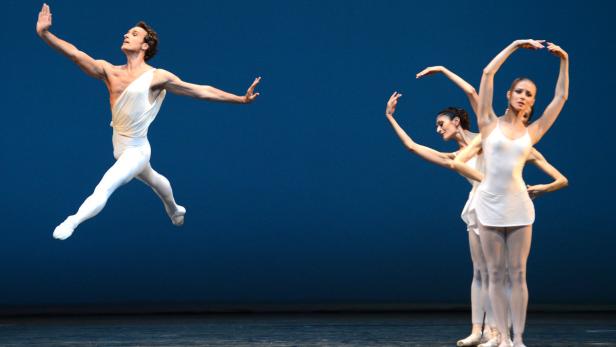 Ein männlicher Balletttänzer springt vor drei Tänzerinnen in weißen Kostümen.
