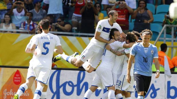 Italienische Fußballspieler feiern ein Tor, während ein uruguayischer Spieler enttäuscht dreinblickt.