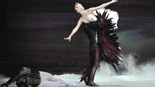 Eine Ballerina in einem schwarzen und roten Tutu tanzt, während ein Tänzer am Boden liegt.