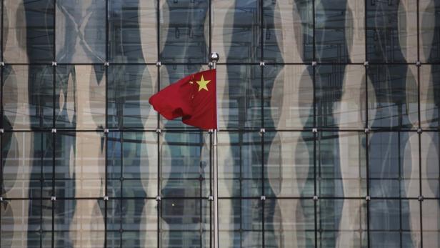 Die chinesische Nationalflagge weht vor einem modernen Glasgebäude.