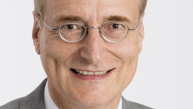 Ein lächelnder Mann mit Brille, Anzug und Krawatte vor einem weißen Hintergrund.