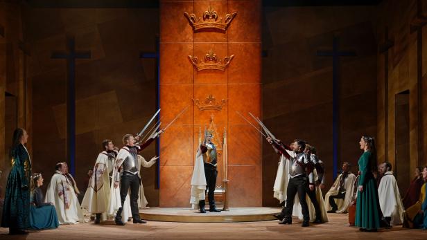 Eine Theaterszene mit einem König auf einem Thron, umgeben von Rittern mit Schwertern.