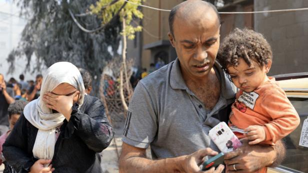 Eine weinende Frau und ein Mann, der ein kleines Kind durch einen zerstörten Ort im Gazastreifen trägt
