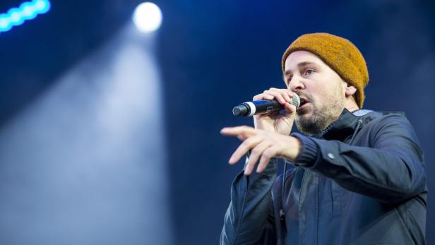 Ein Mann mit Mütze singt in ein Mikrofon auf einer Bühne.