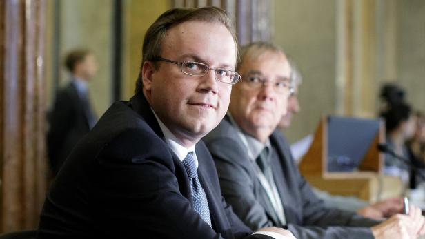 Ein Mann mit Brille und Anzug sitzt an einem Tisch mit anderen Personen.