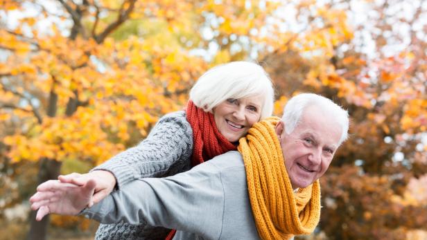 Ein älteres Paar hat Spaß im Herbstlaub, die Frau reitet Huckepack.