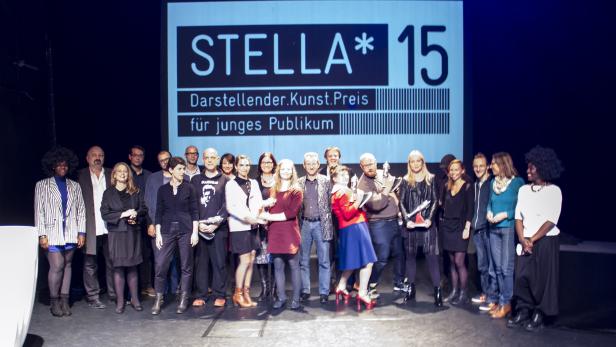 Eine Gruppe von Menschen posiert vor dem „Stella*15 Darsteller.Kunst.Preis für junges Publikum“-Banner.