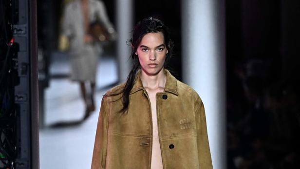 Ein Model auf dem Laufsteg, gekleidet in eine Jacke, weite Hose und Loafer, mit einer Tasche in der Hand.