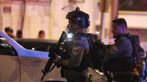 Zwei israelische Polizisten stehen nachts neben einem Polizeiauto.