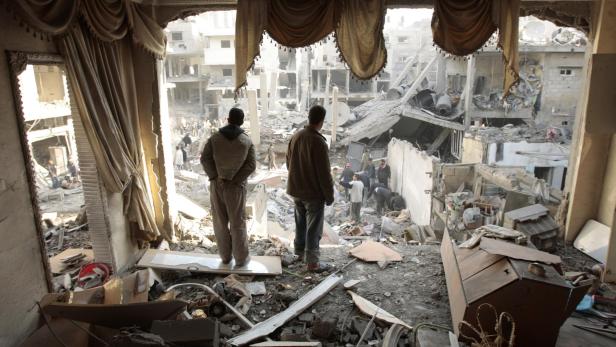Palestinians look at a house destroyed after an Israeli air strike in Gaza City