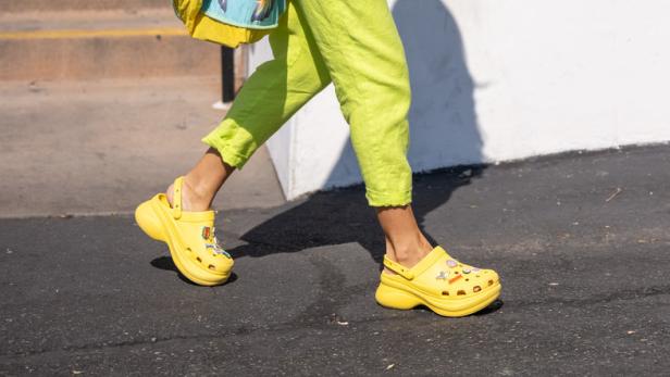 Heidi Klum in einem hellgrünen Overall, gelben Crocs und mit einer bunten Tasche über der Schulter.
