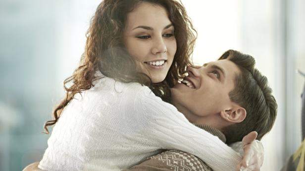 Eine junge Frau umarmt einen Mann und lächelt ihn an.