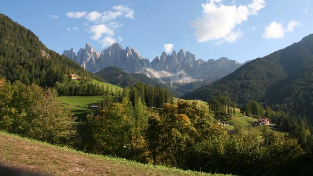 Blick auf die Geislerspitzen in den Dolomiten, umgeben von grünen Hügeln und Wäldern.