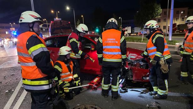 Feuerwehrleute arbeiten nachts an einem roten Unfallwagen.
