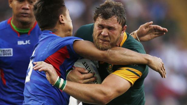 Beim Rugby umklammert ein Spieler in Grün einen Spieler in Blau.