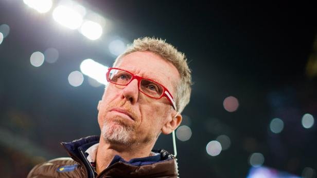 Ein Mann mit roten Brillengläsern und brauner Jacke blickt nach oben.