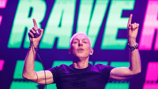 H. P. Baxxter mit erhobenen Händen steht vor einer großen „RAVE“-Leuchtschrift.